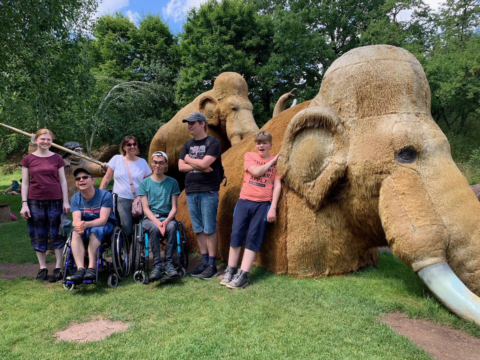 Eine Gruppe Menschen steht in einem Park vor einem Mammut