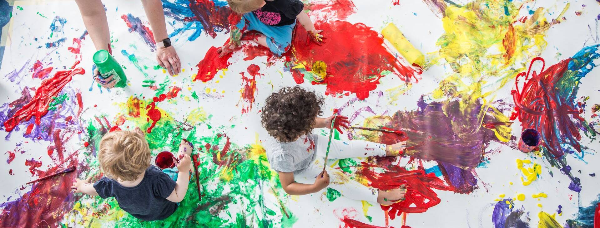 Eine Gruppe von kleinen Kinder spielt mit Fingerfarben auf einem großen Blatt.