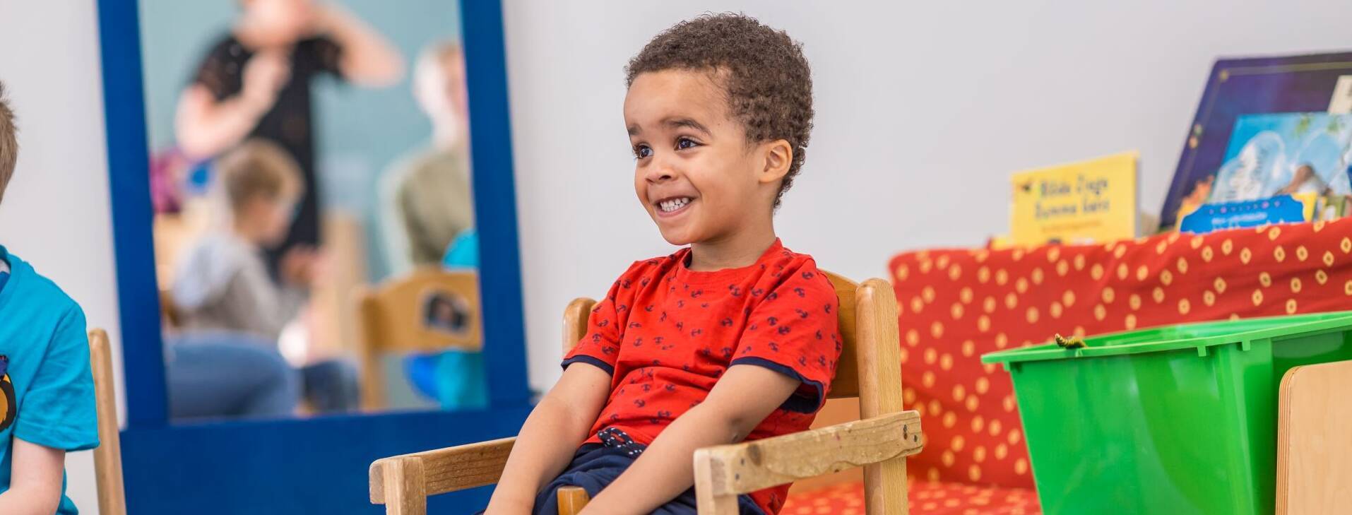 Ein Kind grinst sehr fröhlich auf ein einem Holzstuhl.