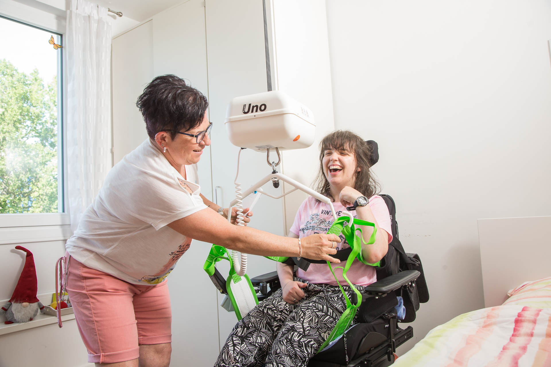 Betreuerin hilft Bewohner mit Rollstuhl mit einem Gerät beim Aufstehen